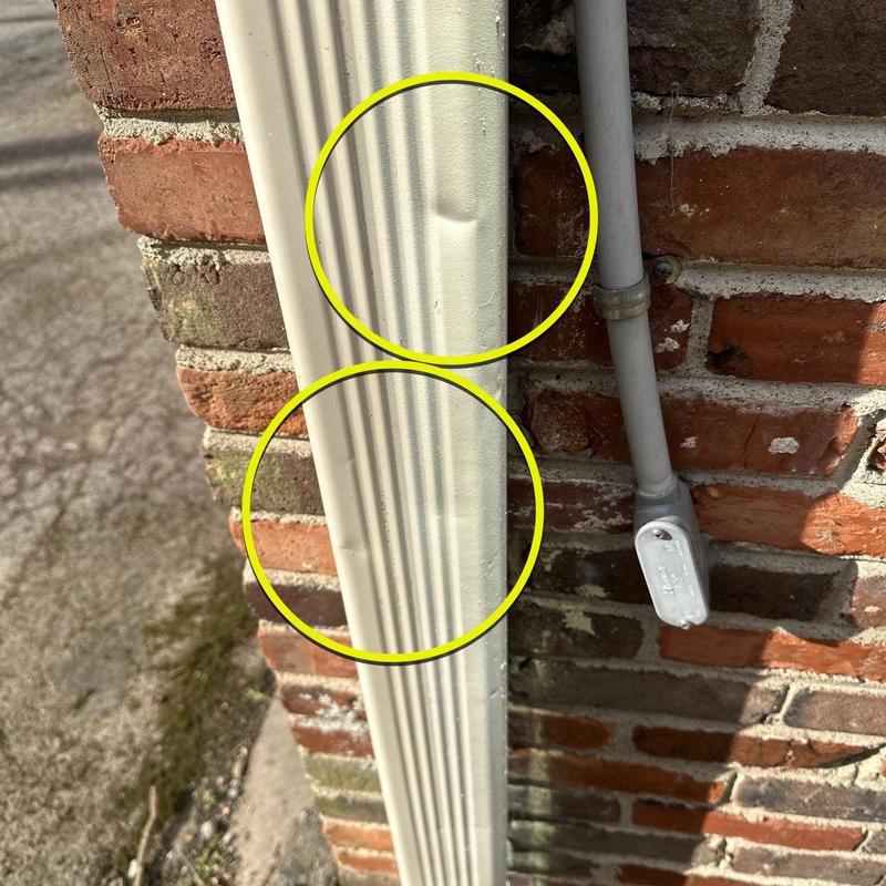 Downspout dents on exterior brick wall near conduit box