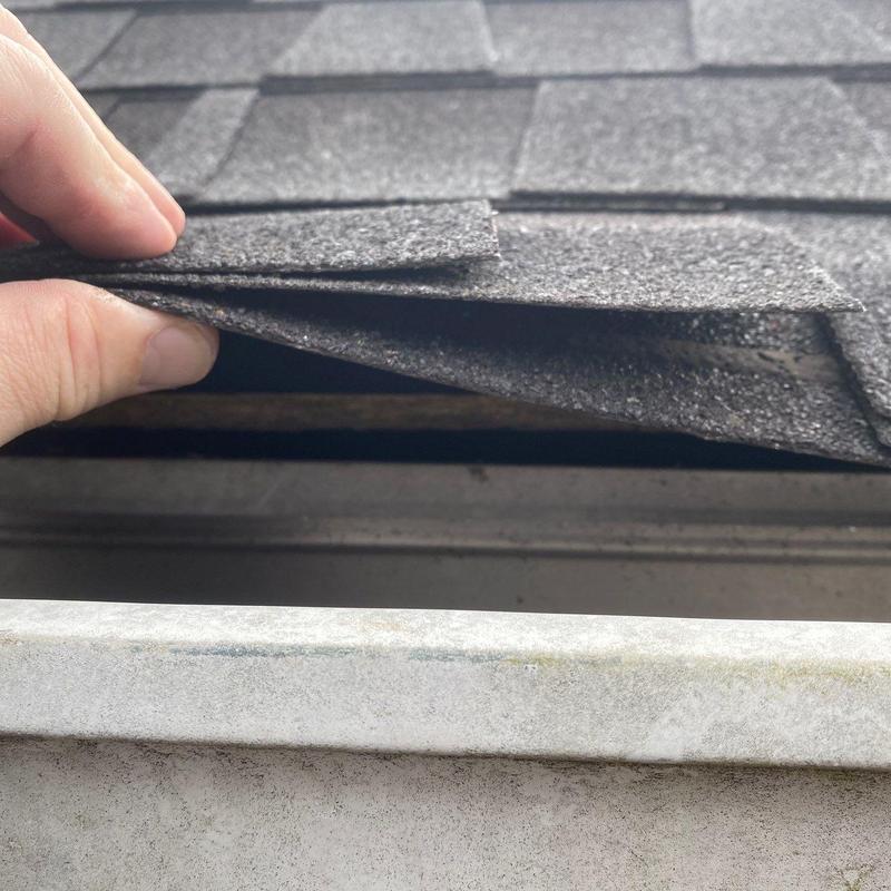 Asphalt shingle lifted for roof inspection near gutter