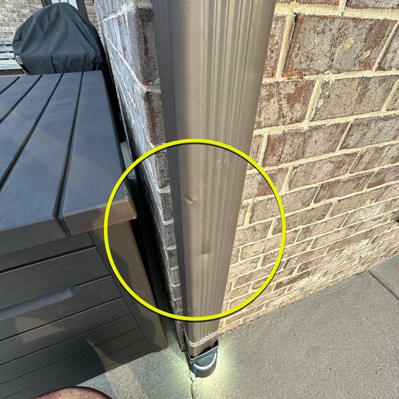 Downspout with visible dents near brick wall