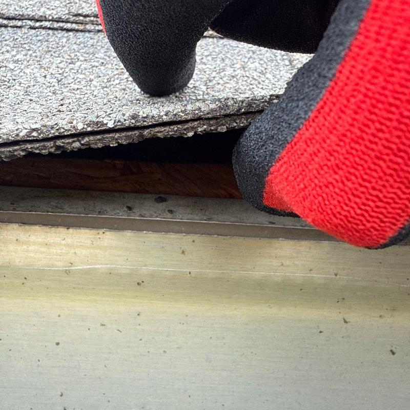 Asphalt shingles lifted for roof inspection with red gloves