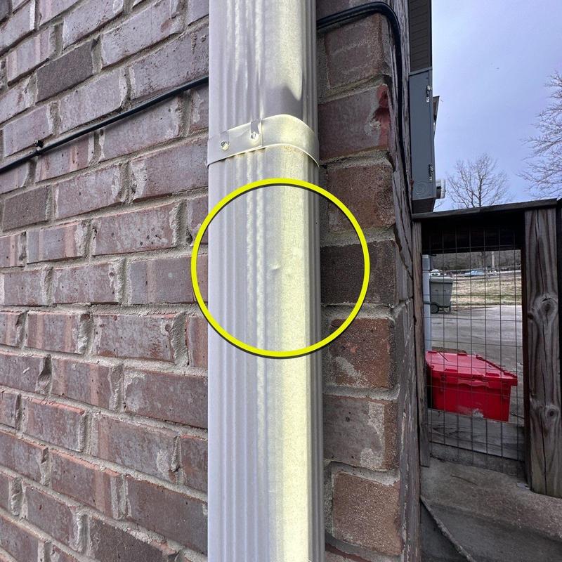 Downspout pipe dent highlighted on brick wall exterior
