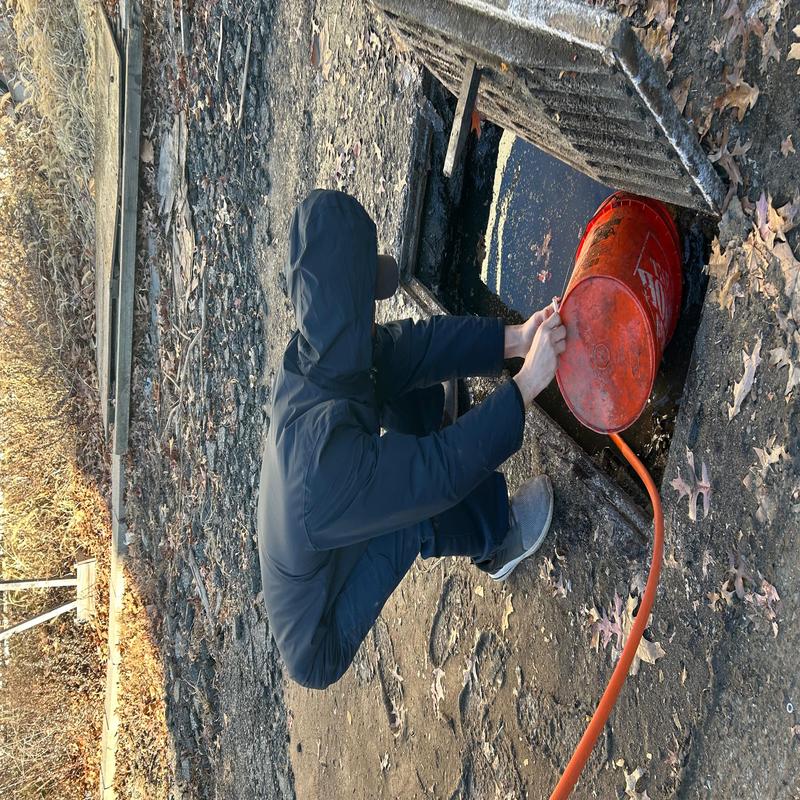 Storm catch basin cleaning with orange hose on commercial site