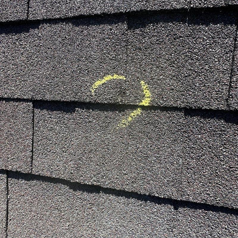Asphalt roof shingle with hail damage marked in yellow