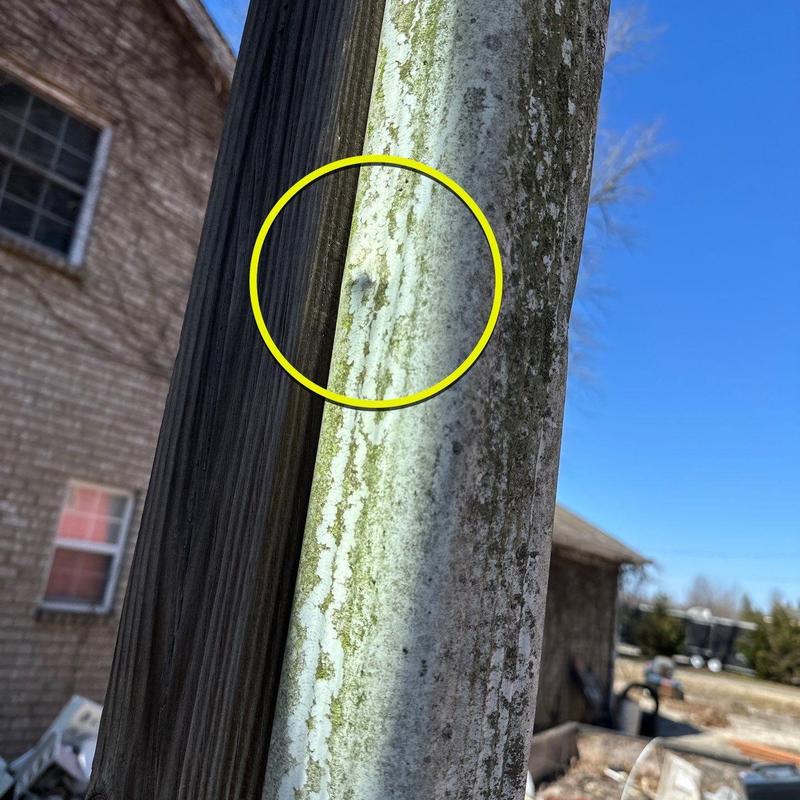 Metal downspout with hail dent marked by yellow circle