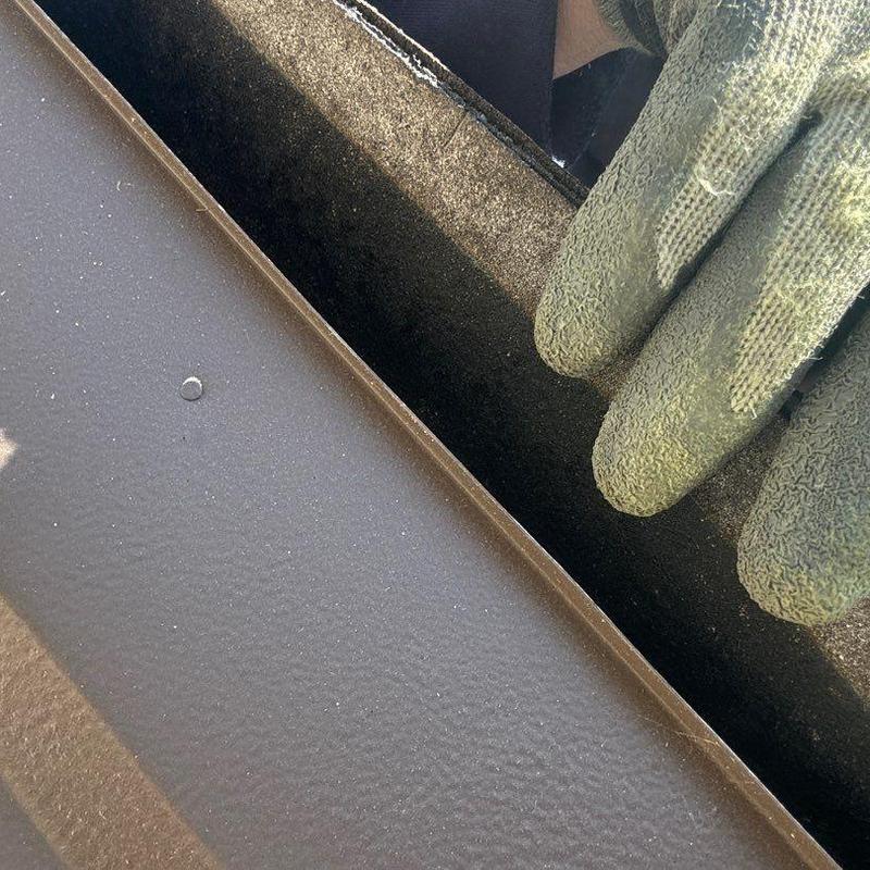 Metal roof flashing close-up with gloved hand inspecting