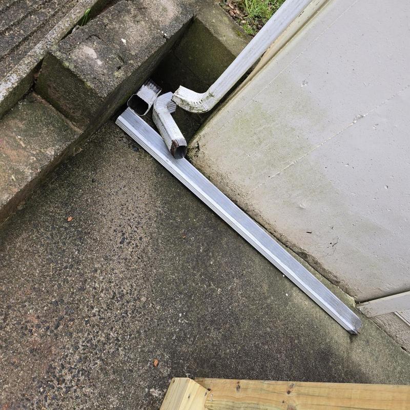 Downspout disconnected on concrete corner near wall