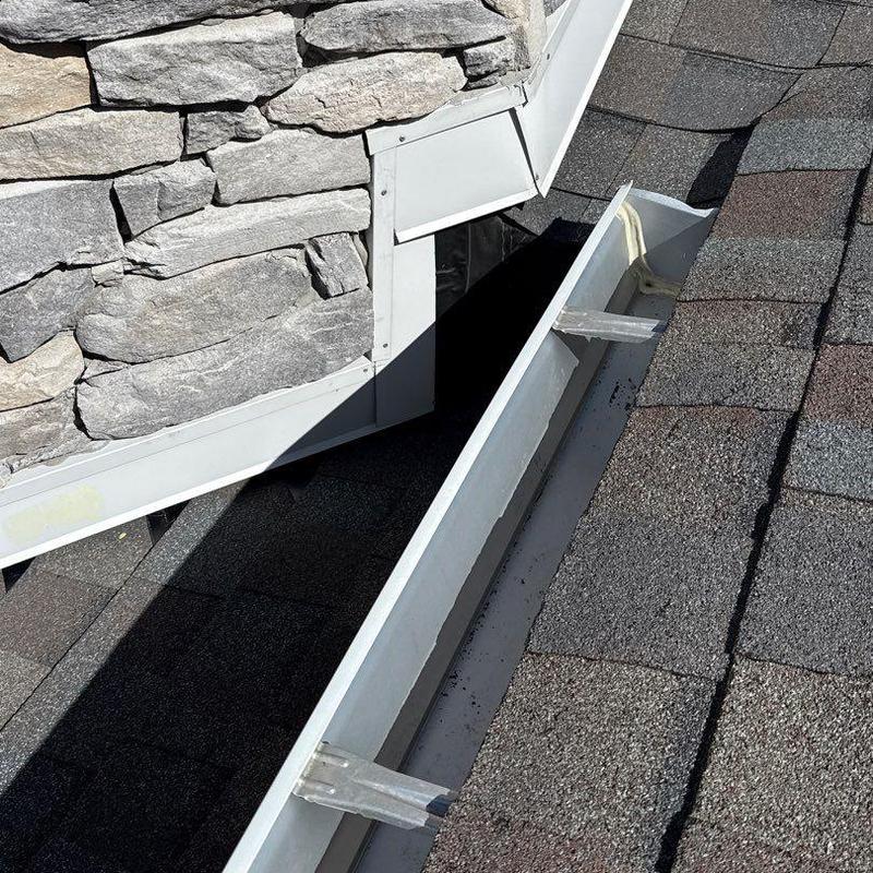 Roof gutter and flashing on shingle roof near stone wall