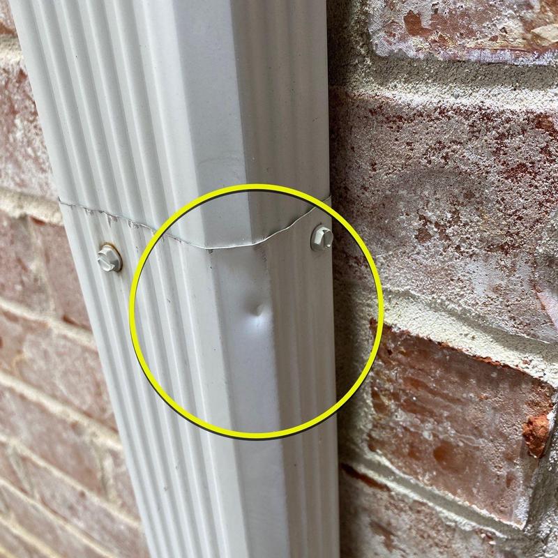 Downspout dent near joint fastened to brick wall