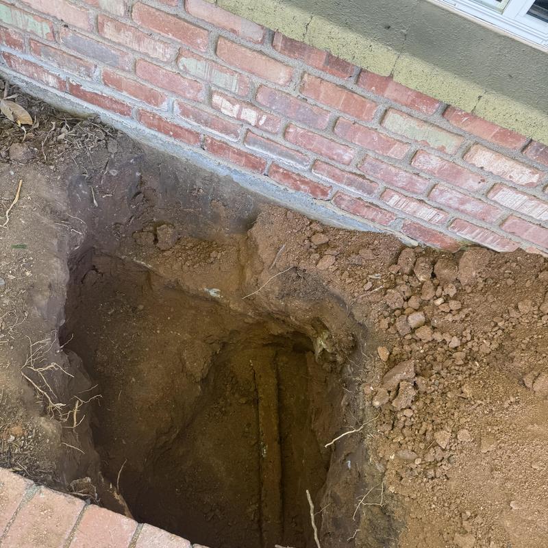 Cleanout sewer pipe with excavation hole next to house wall