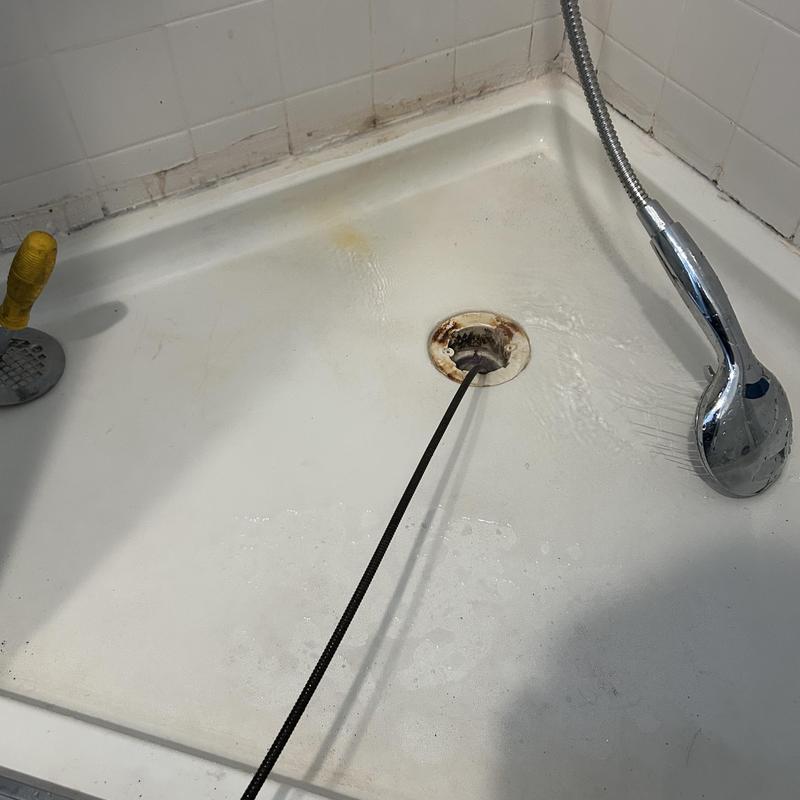 Shower drain cleaning with plumbing snake tool in tub