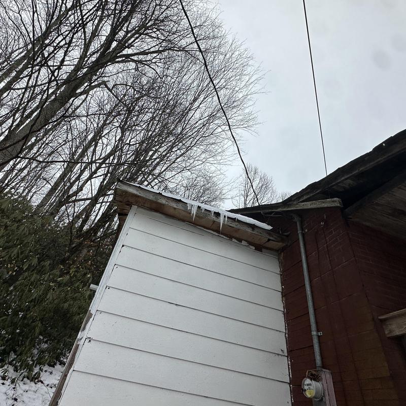 Roof shingle edge with icicles on white siding wall