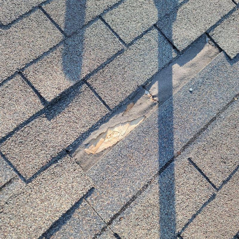 Asphalt roof shingles with wind damage and exposed wood Asphalt roof shingles with wind damage and exposed wood