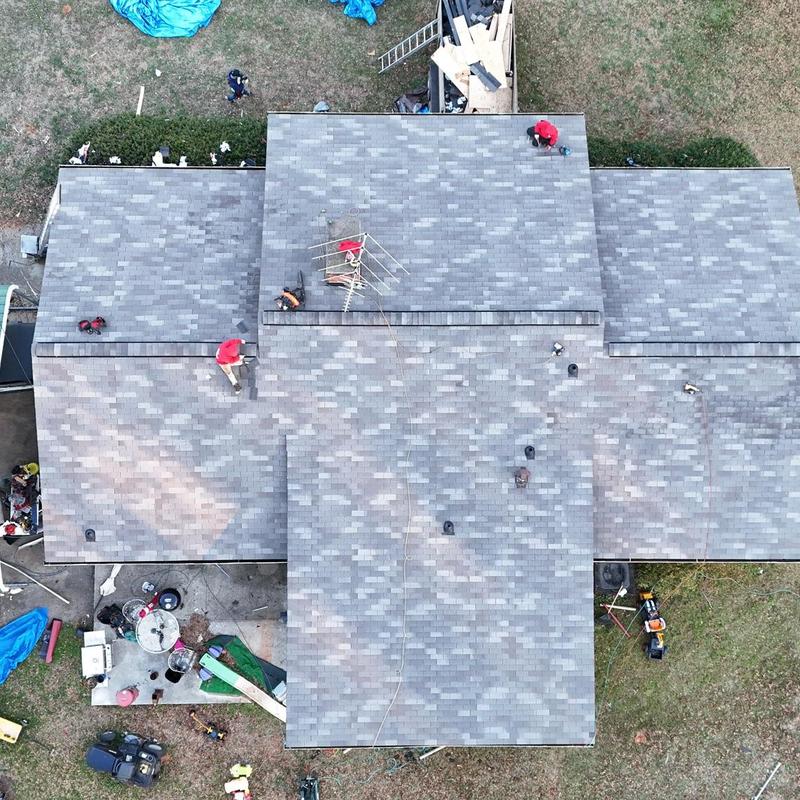 Asphalt shingle roof with workers installing decking boards