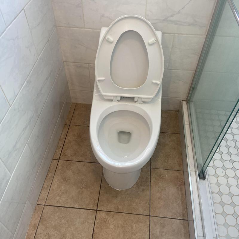 Toilet with open lid in tiled bathroom corner