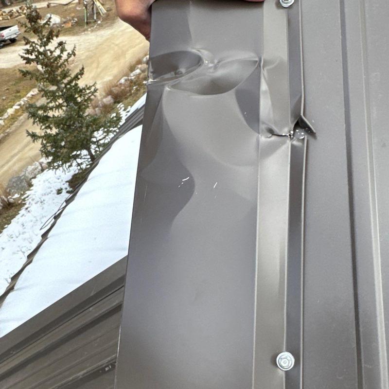 Metal roof panel with dented damage near flashing