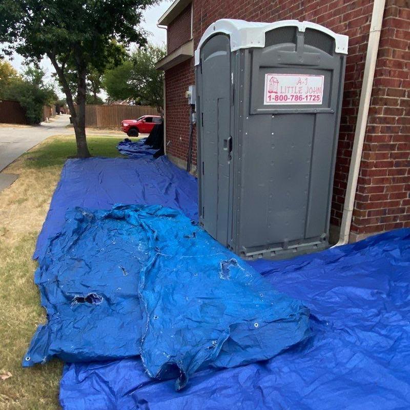 Blue roof protection tarps beside brick house and porta-potty