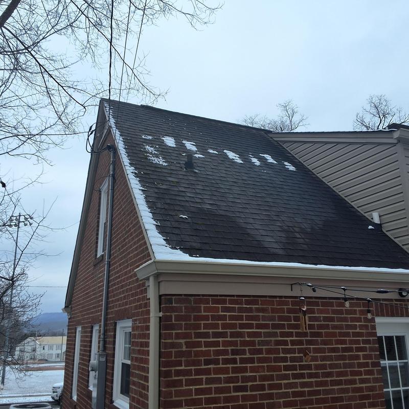 Black asphalt shingle roof with snow patches and algae
