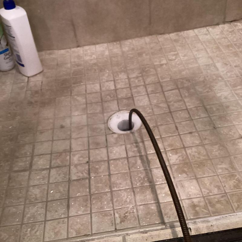Shower drain cleaning with plumbing snake in tile shower