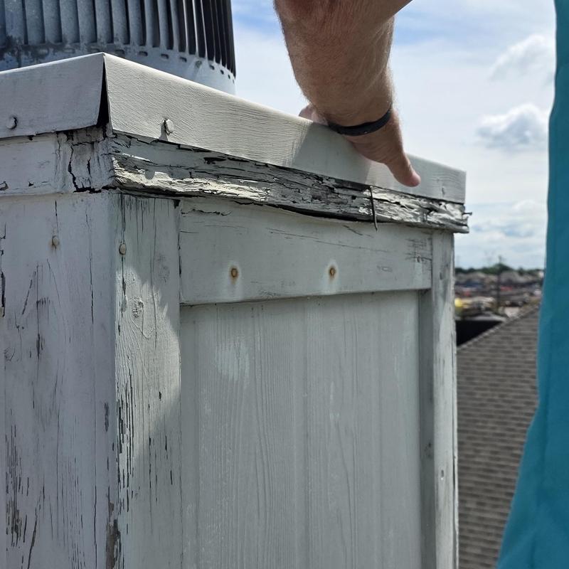 Damaged wooden rooftop vent cover with peeling paint