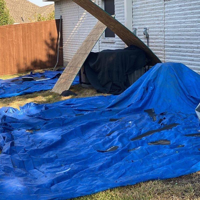 Roofing shingles removed on blue tarp near house exterior