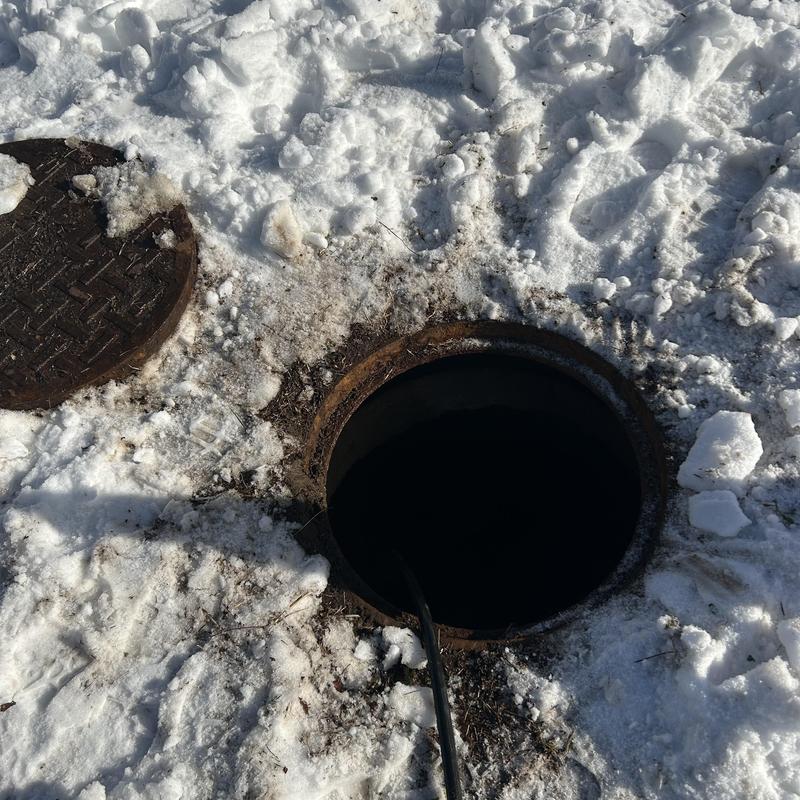 Sewer pipe ice clog inspection with open manhole in snow