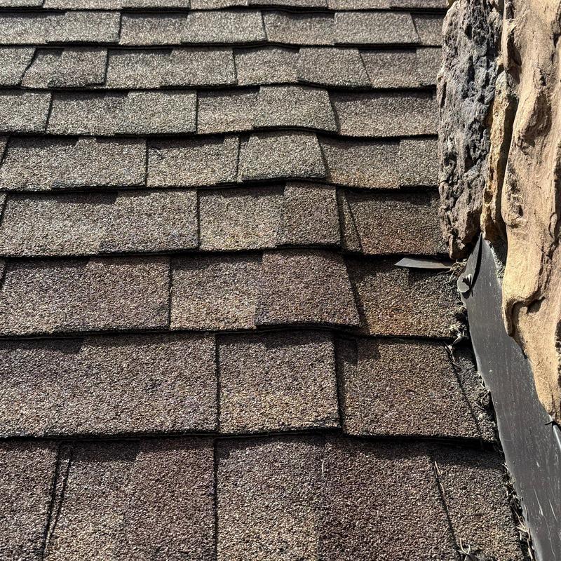 Asphalt shingle roof inspection near chimney flashing