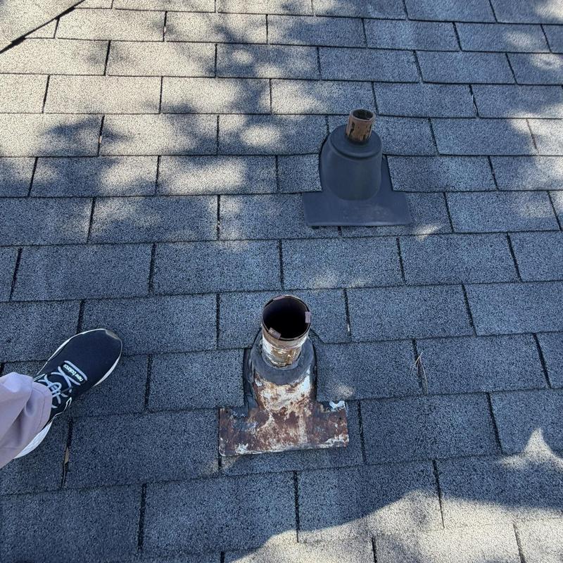 HVAC vent pipes on asphalt shingle roof with foot nearby