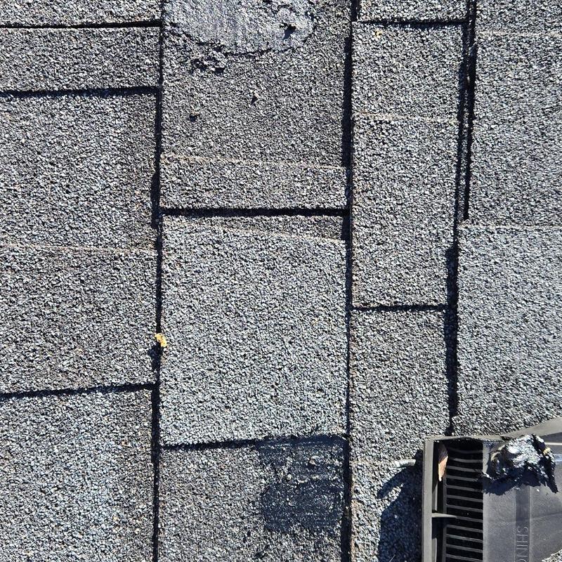 Roof shingles showing hail and wind damage near vent