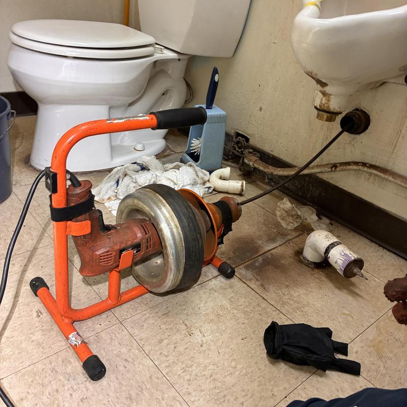 Urinal drain cable machine clearing clog in restroom