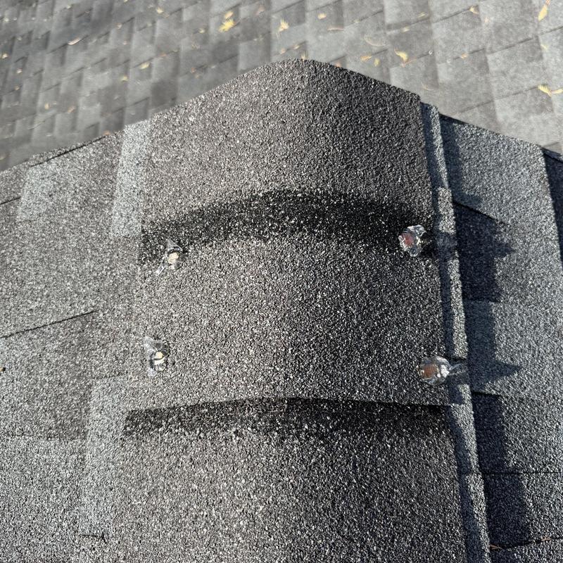 Roof ridge cap with sealed exposed nails on charcoal shingles