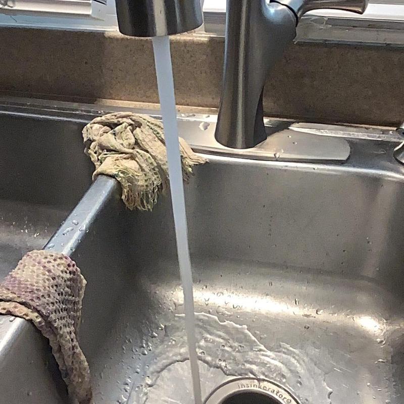 Kitchen sink drain with water running and cleaning cloths