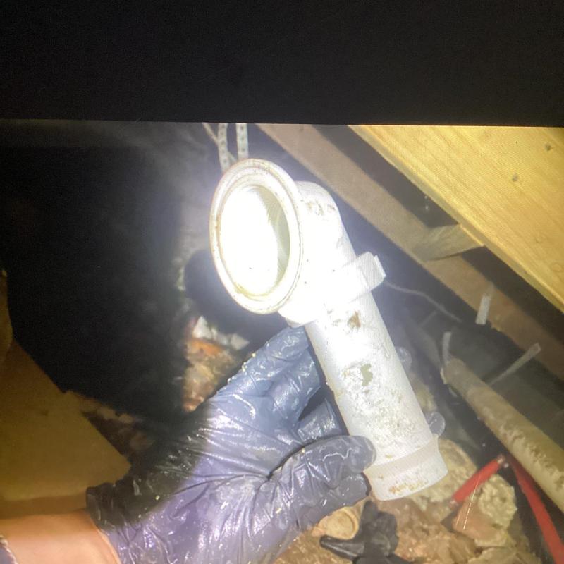 Shower drain pipe held by gloved hand in crawl space