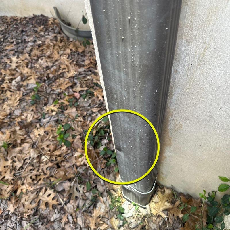 Downspout dent with surrounding leaf debris near foundation wall