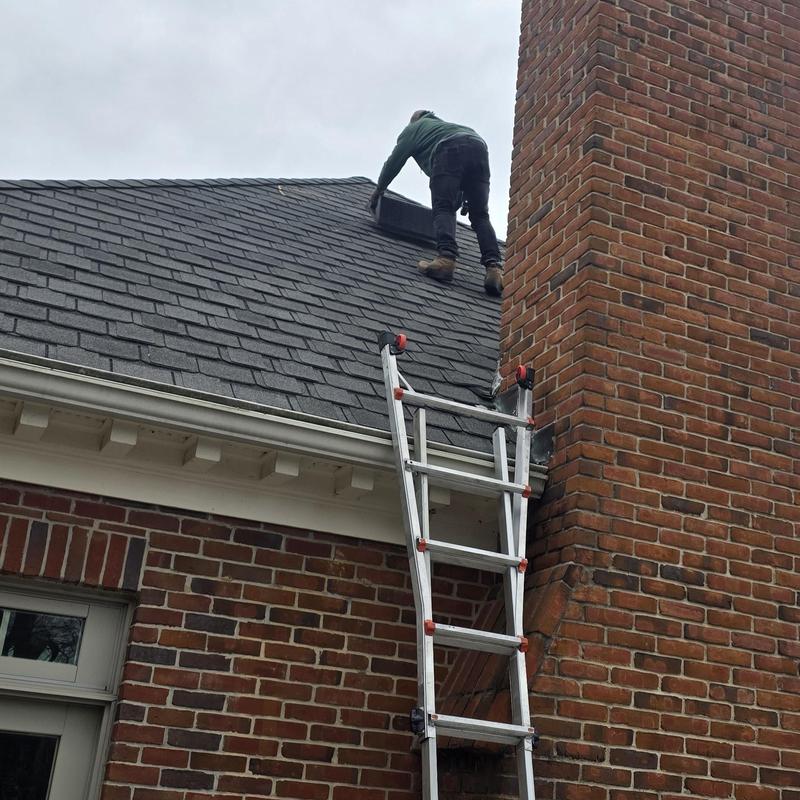 Asphalt shingle roof with ladder and worker near chimney