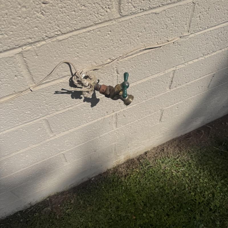 Outdoor hose bib valve attached to brick wall with wire