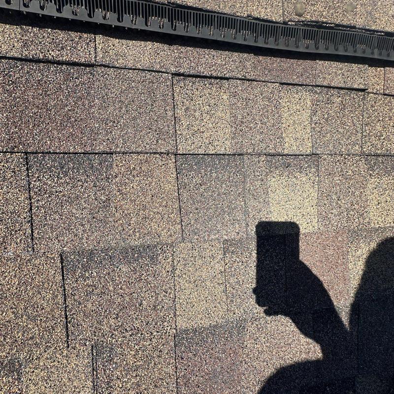 Asphalt roof shingles with visible hail damage and shadow