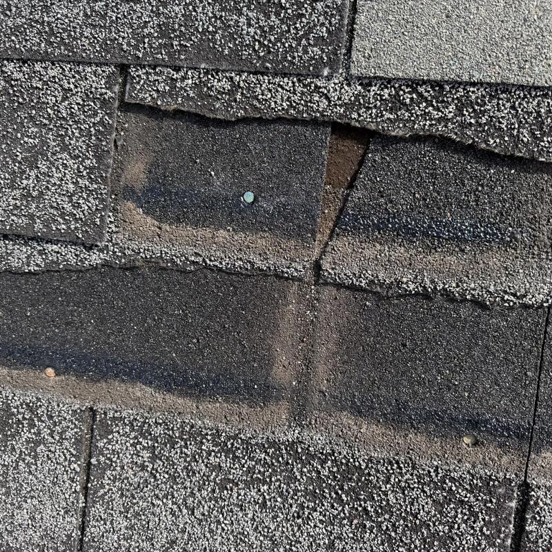 Damaged asphalt shingles with nail exposed on roof