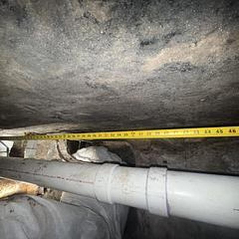 PVC sewer line under home with measuring tape
