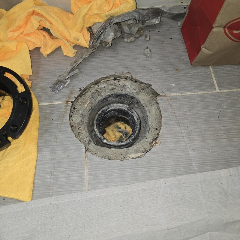 Broken closet flange on tiled floor with tools nearby