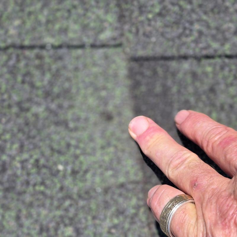 Asphalt roof shingles close-up showing hail damage and hand
