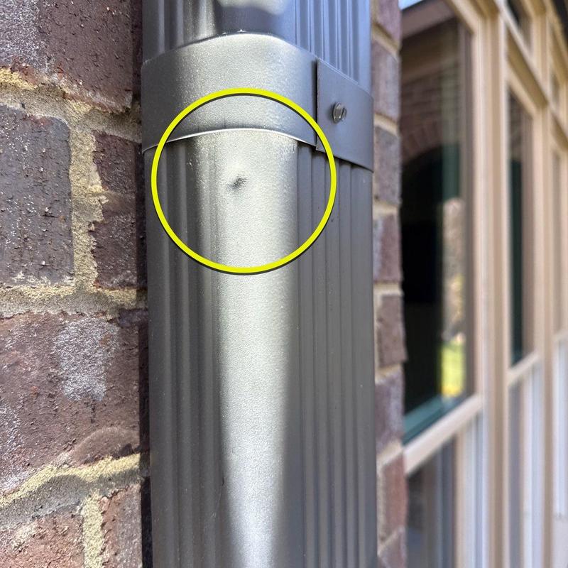 Downspout dent circled on exterior building wall