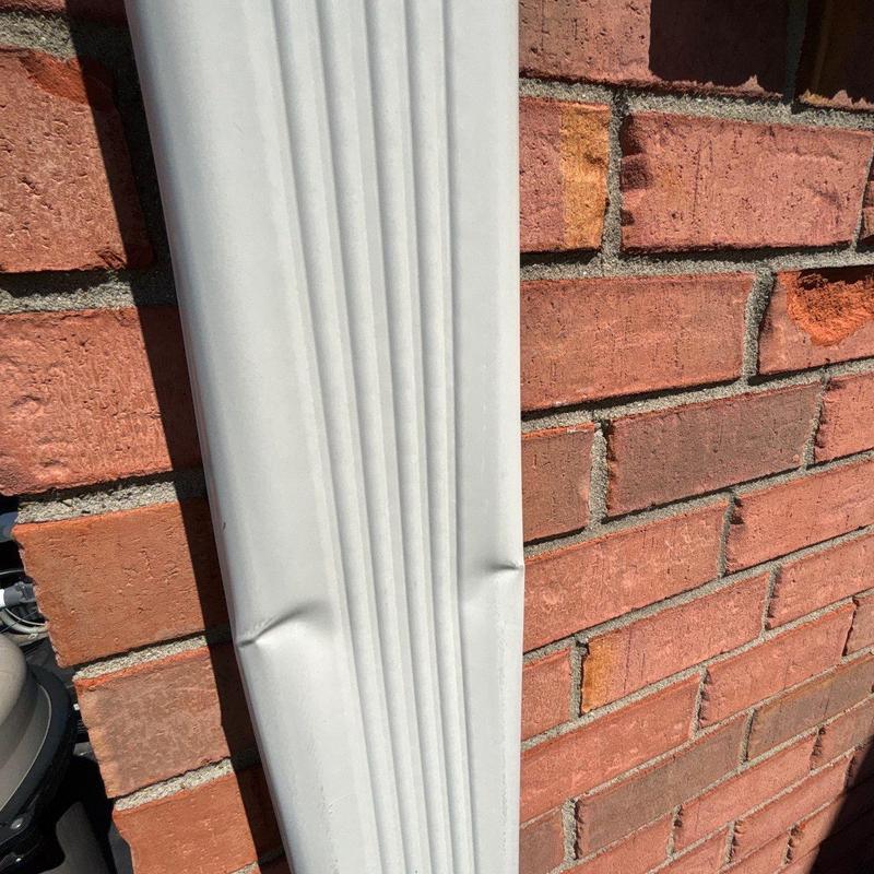 Vinyl downspout with minor dents on brick wall
