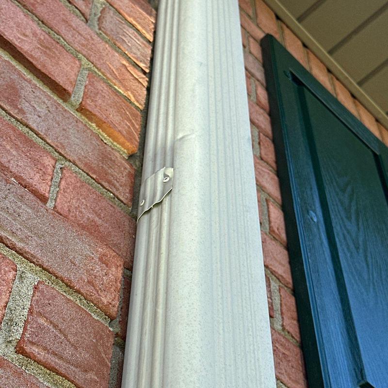 Vinyl downspout with detached mounting bracket on brick wall