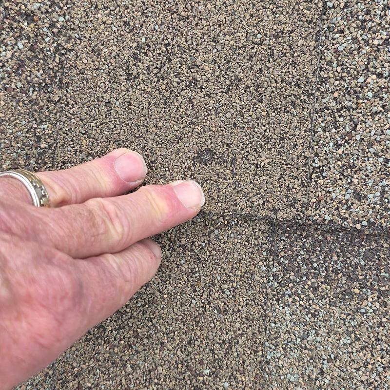 Roof shingles with hail damage close-up and fingers for scale