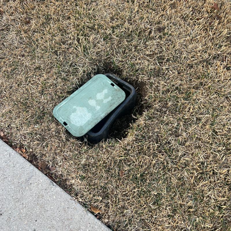 Water main valve box partially buried in dead grass