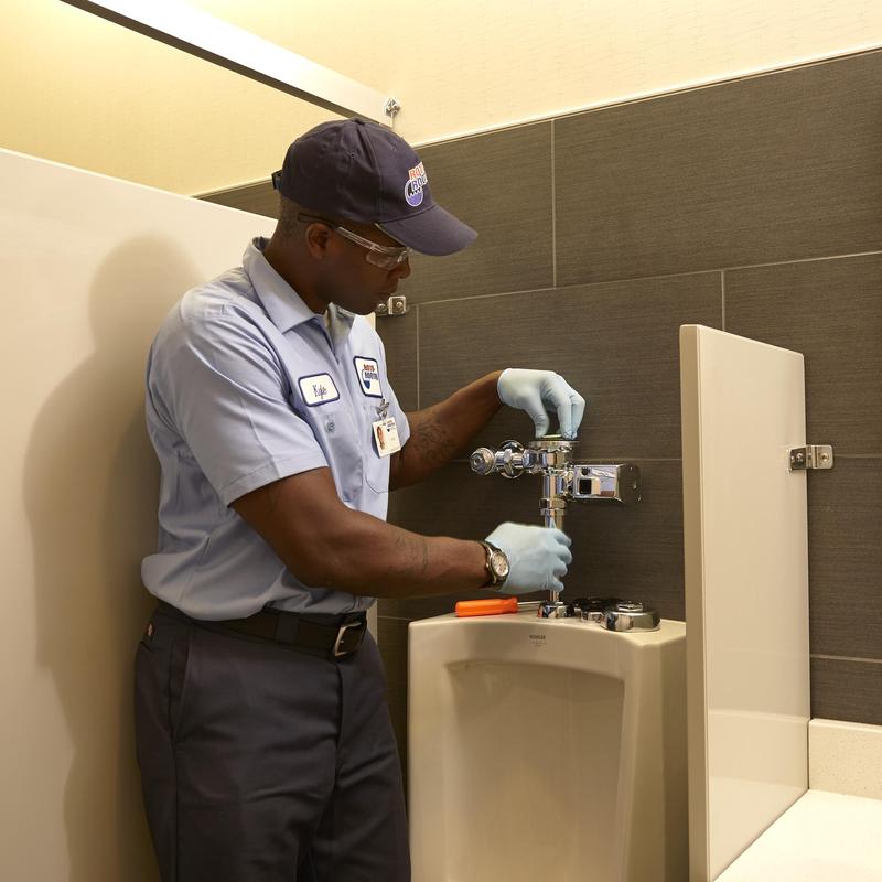 Urinal flush valve installation by plumber in restroom