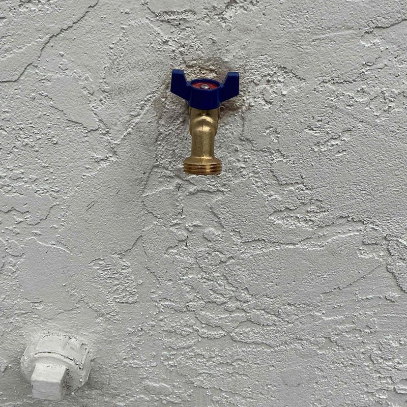 Hose bib with blue handle on textured wall