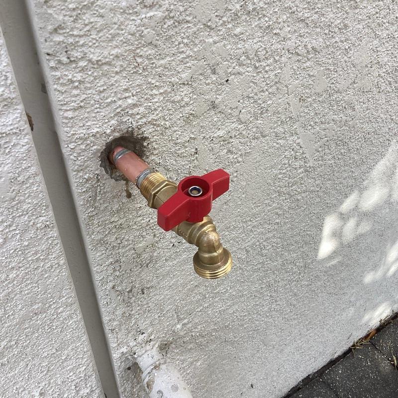Quarter turn hose bib with red handle on exterior wall