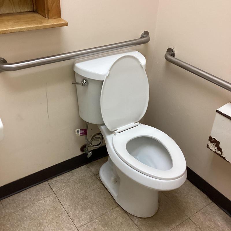 Toilet with open lid and grab bars in restroom corner