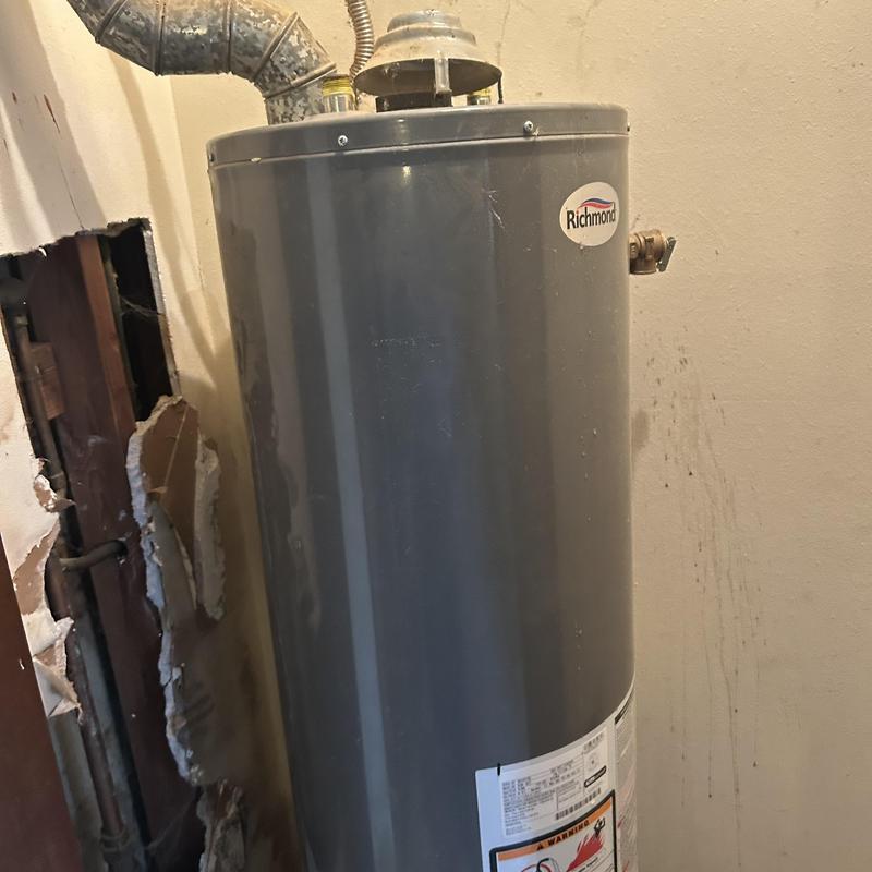 Water heater with vent pipe and damaged wall nearby